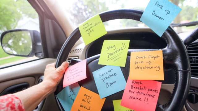 Working parent places sticky notes with reminders on a car steering wheel.