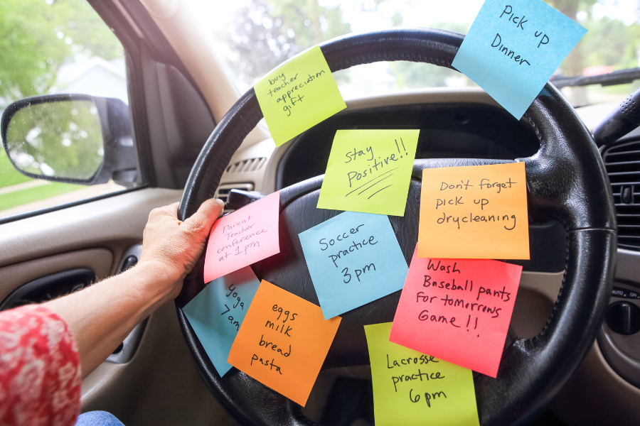 Working parent places sticky notes with reminders on a car steering wheel.