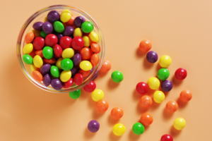 A dish of Skittles on an orange backdrop.