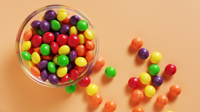 A dish of Skittles on an orange backdrop.